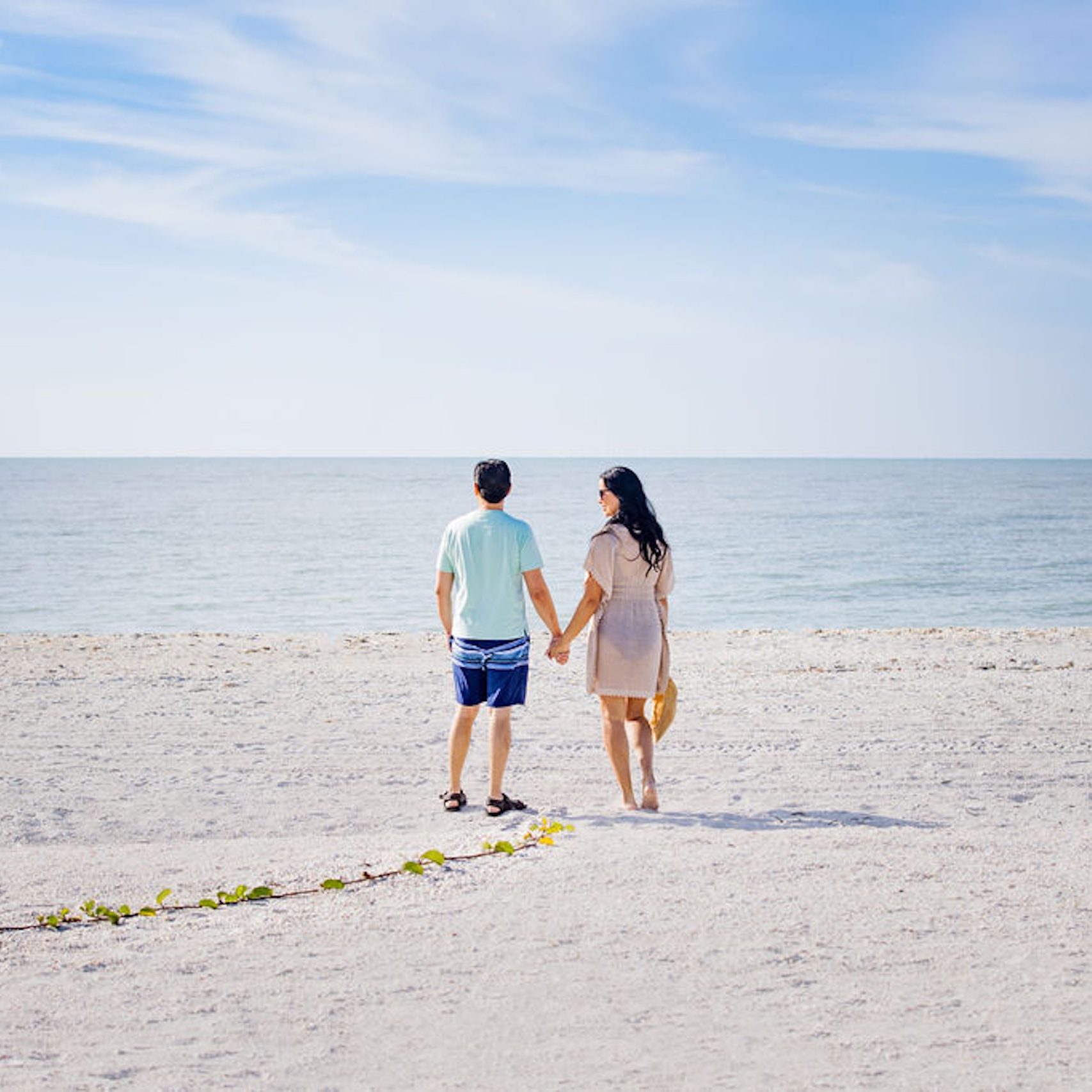 Two people holding hands on a beach in the distance